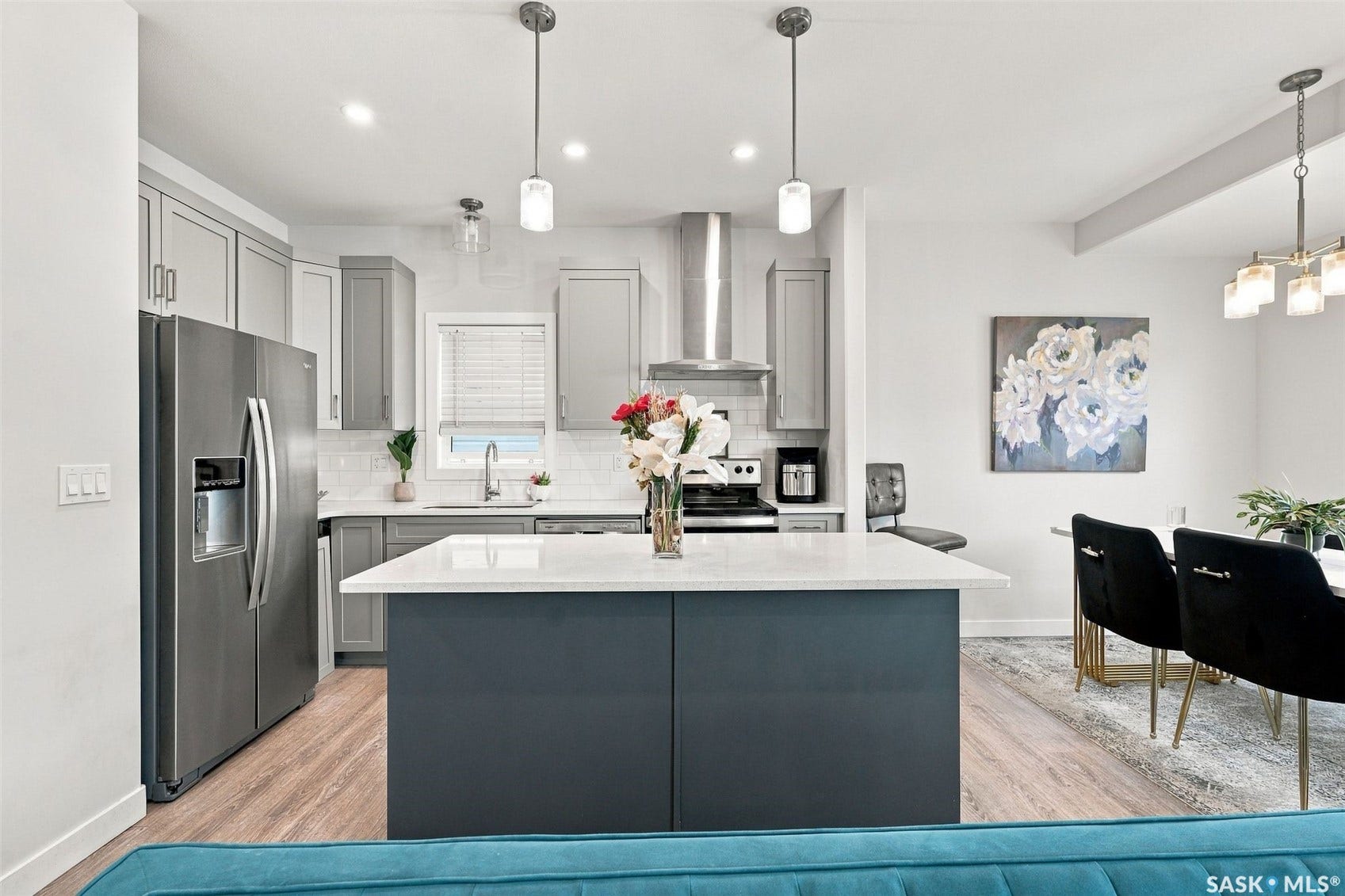 Stainless steel appliances, light wood-finish flooring, grey cabinetry, white countertops, and a kitchen island with pendant lighting