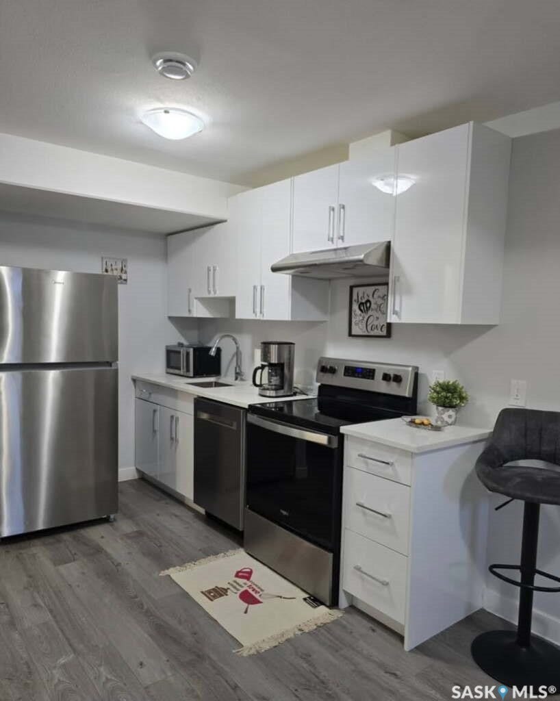Kitchen featuring stainless steel appliances, white cabinetry, light-toned countertops, wood-finish flooring, and a breakfast bar