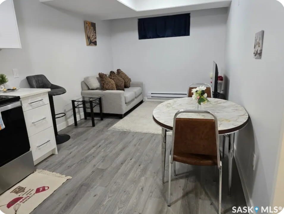 Wood-finish flooring throughout, white cabinetry with handle pulls, stainless steel range, and a breakfast bar with a single stool