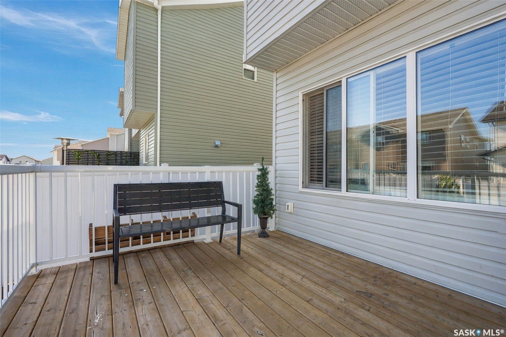 Wood-finish deck with white railing, featuring light-colored siding and large windows