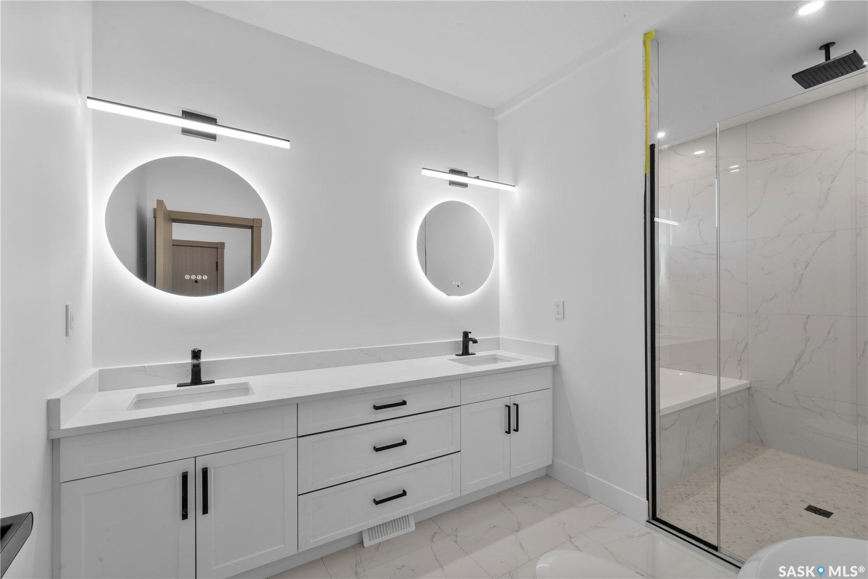 12 Elkwood Cove, Dundurn Rm No SK S7C 0C5 Dual vanity with white cabinetry and matte black hardware, quartz countertops, back-lit round mirrors, and a glass-enclosed shower with a built-in bench