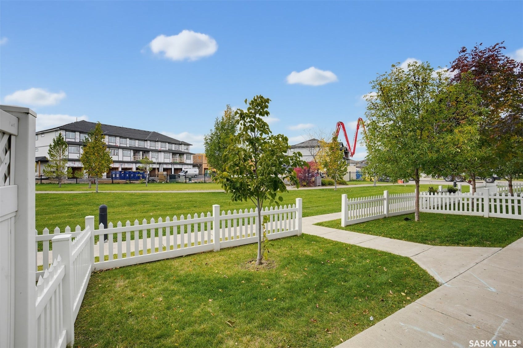 Expansive green space featuring white picket fencing, mature trees, and concrete pathways