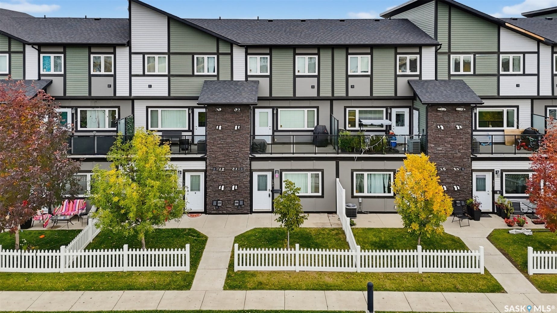 Contemporary multi-level exterior with varied siding, private balconies, and individual front yards featuring picket fences and mature landscaping