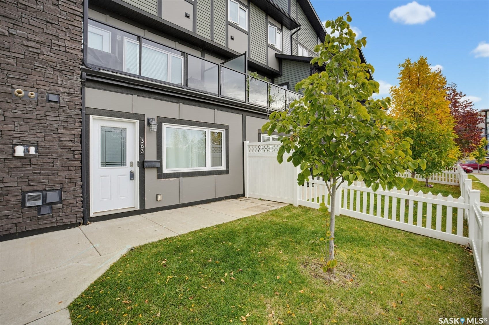 Modern townhouse exterior featuring a white entry door, an exterior wall with stone-look siding, and a fenced front yard with a white picket fence