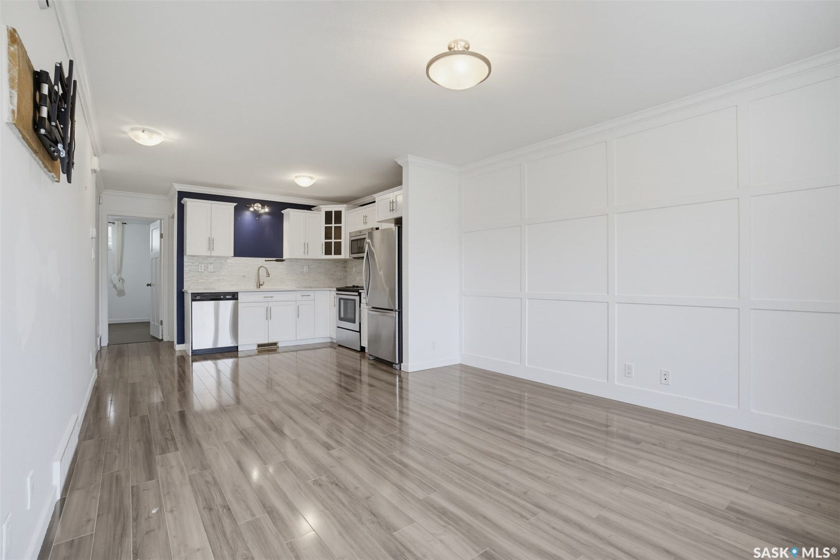 Open-concept layout featuring wood-finish flooring, a kitchen with stainless steel appliances, white cabinetry, and a subway tile backsplash, and a paneled accent wall