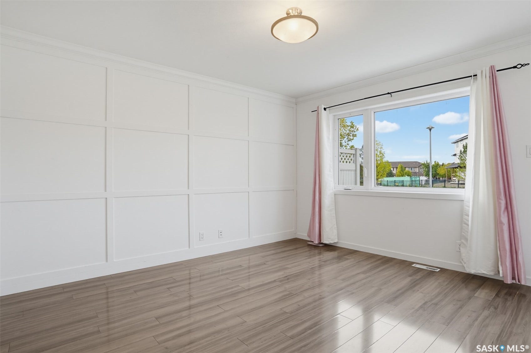 Decorative paneled accent wall, wood-finish flooring, white window trim, and a semi-flush mount ceiling light