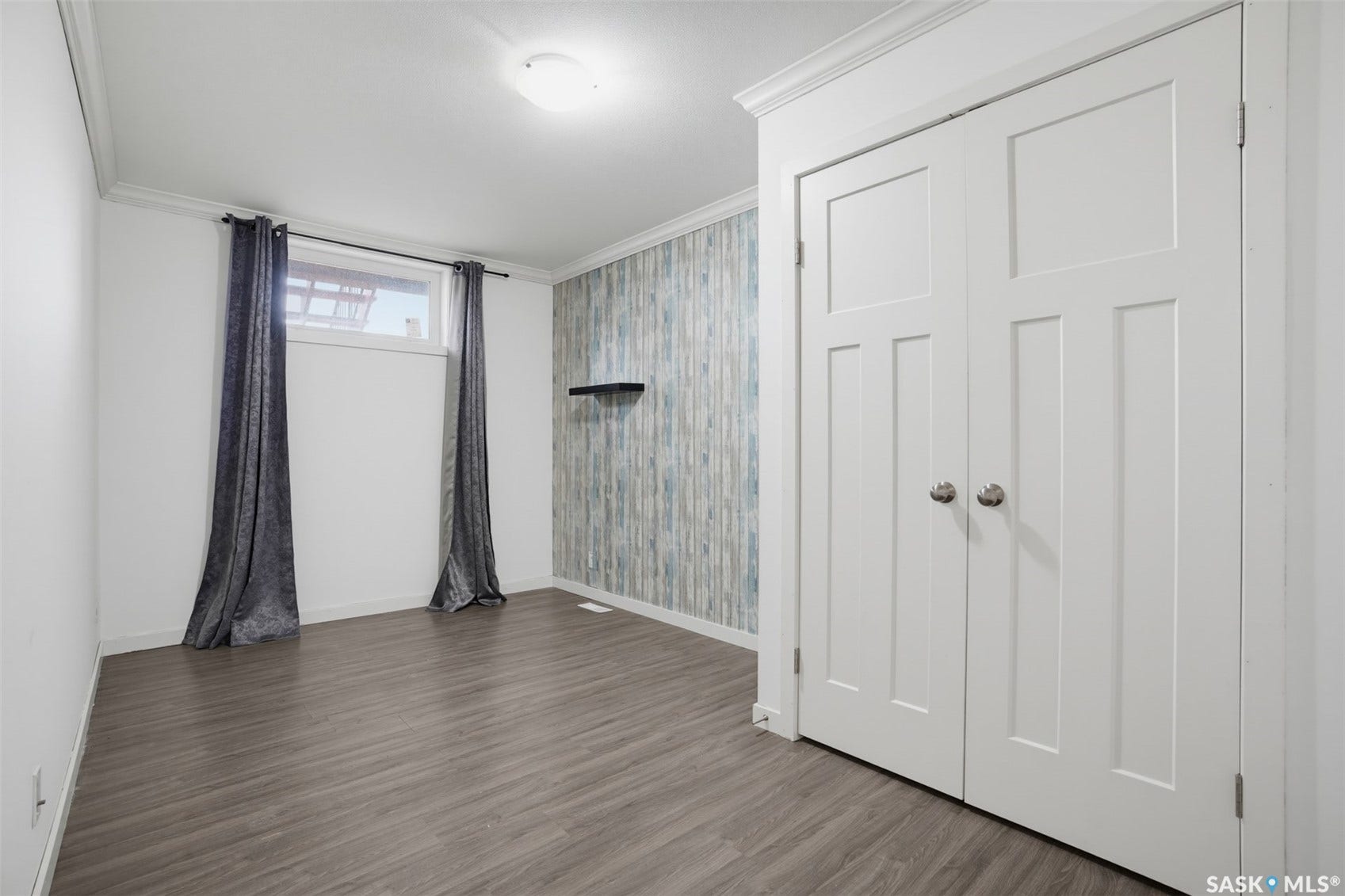 Wood-finish flooring, accent wall with vertical paneling, recessed window, ceiling-mounted light fixture, and white bi-fold doors