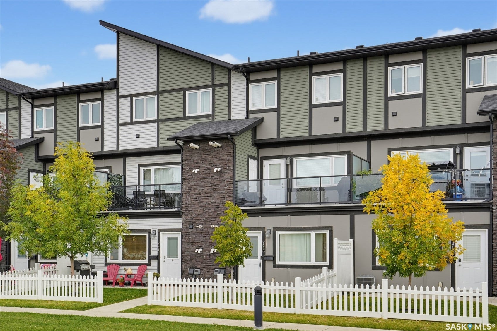 Contemporary exterior with multi-toned siding, stone accent pillar, private balconies with glass railings, and individual fenced yard areas