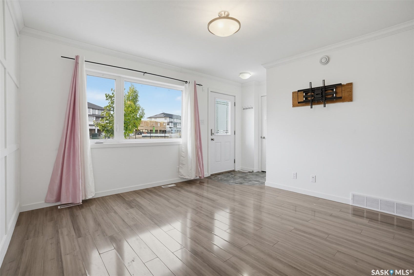 Spacious room with wood-finish flooring, a large window, white trim, and a ceiling-mounted light fixture