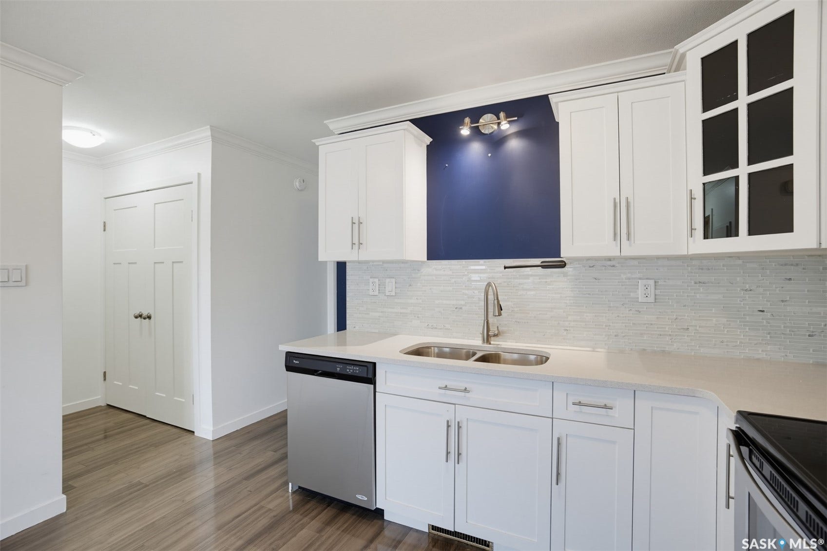 White shaker cabinetry, light-toned countertops, stainless steel dishwasher, glass tile backsplash, and wood-finish flooring
