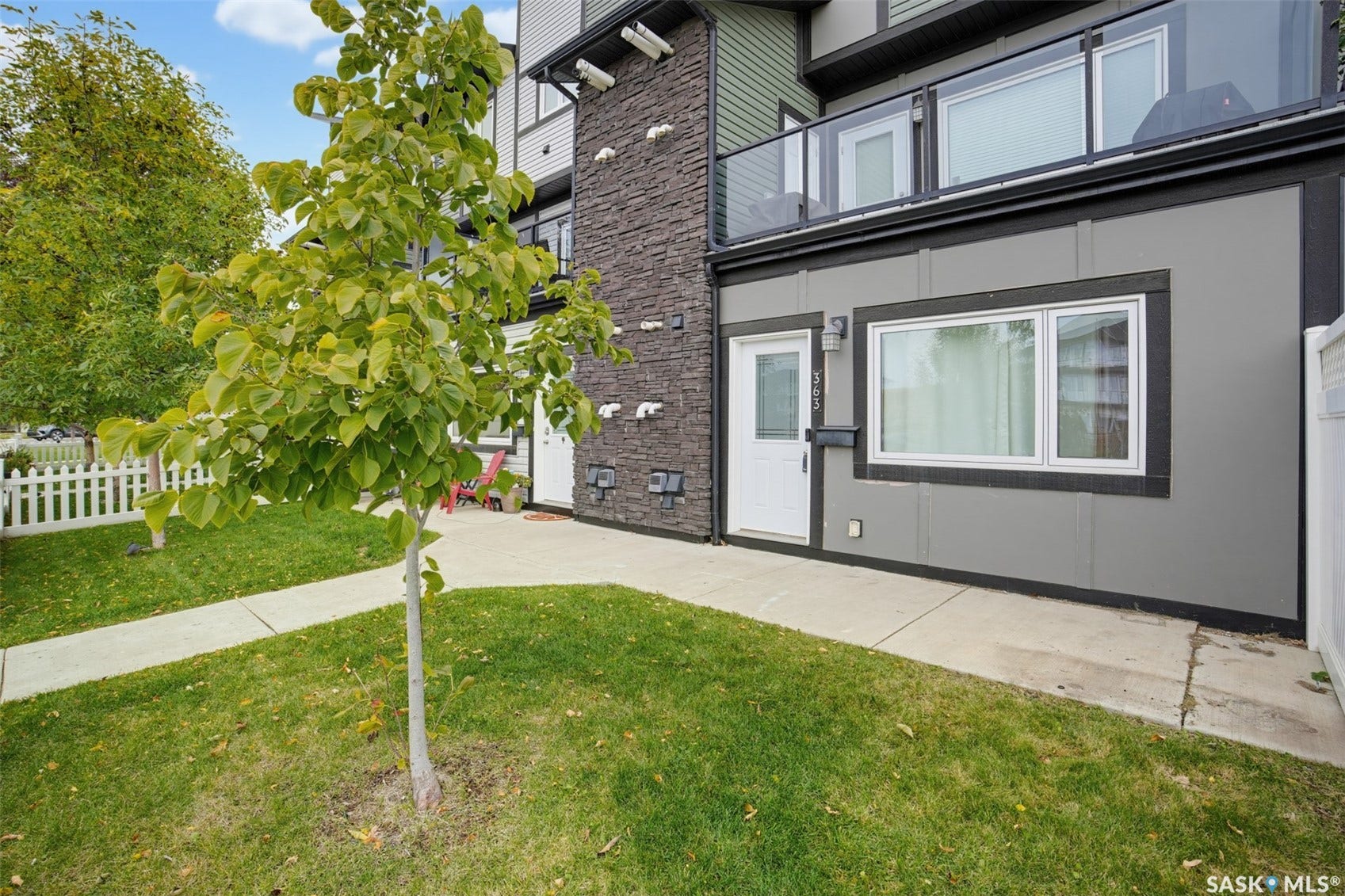 Modern exterior with stone accents, featuring a white entry door and a balcony with a glass railing
