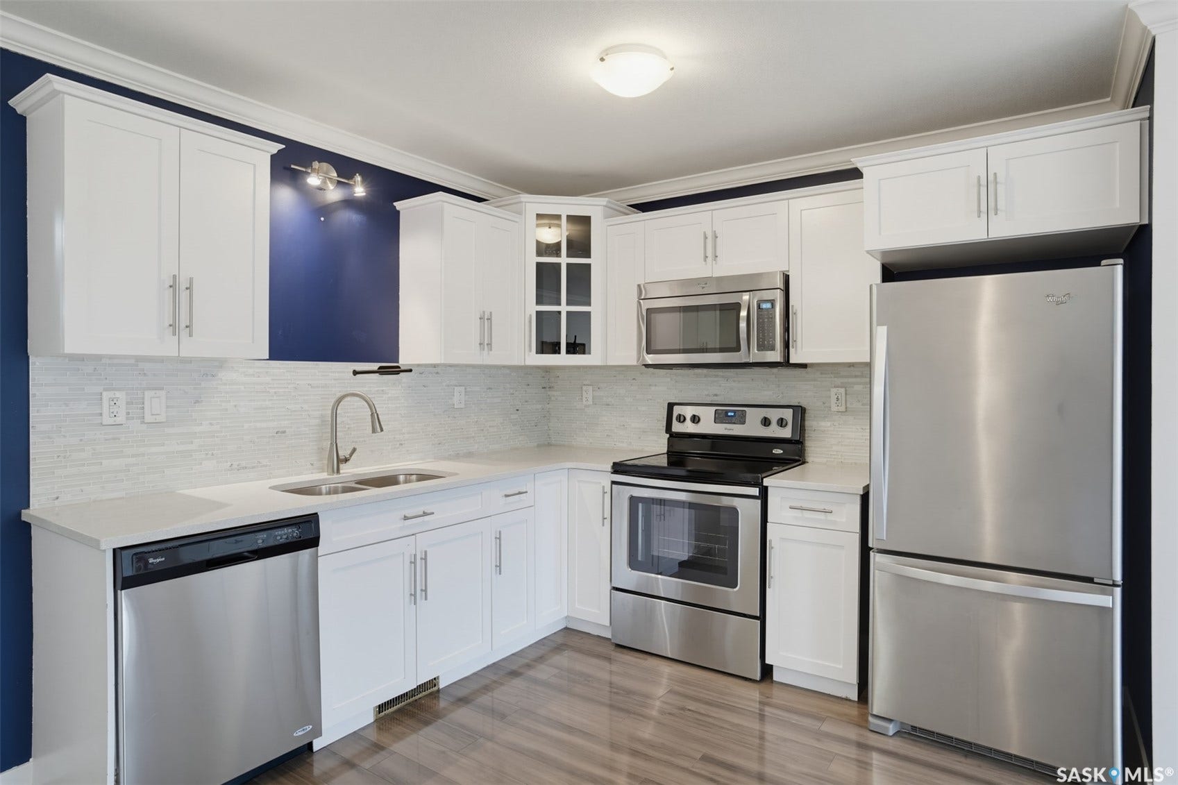 White cabinetry with crown molding, stainless steel appliances, light countertops, mosaic tile backsplash, and wood-finish flooring