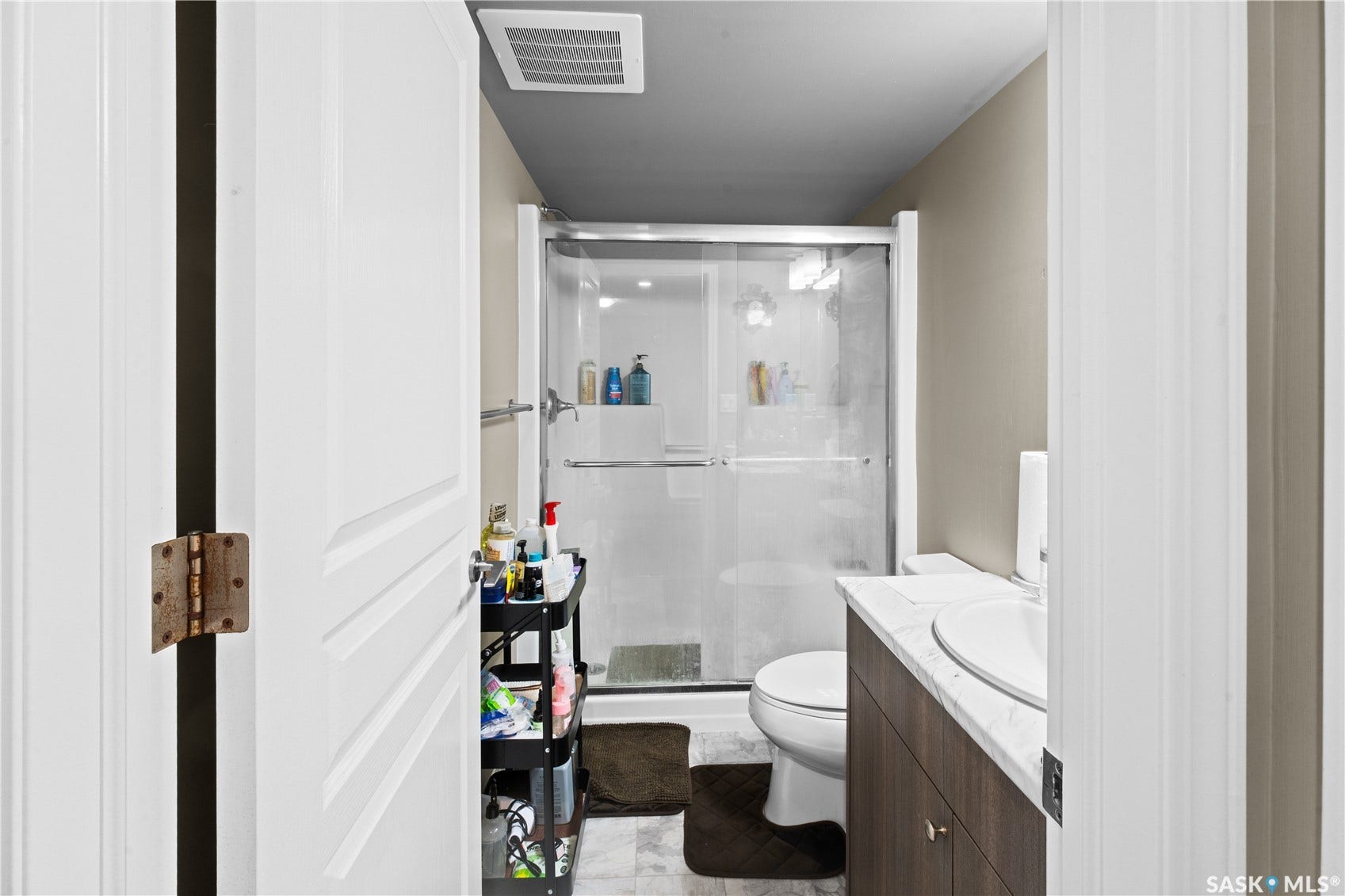 White paneled interior door, glass-enclosed shower, white toilet, wood-finish vanity, and white basin sink