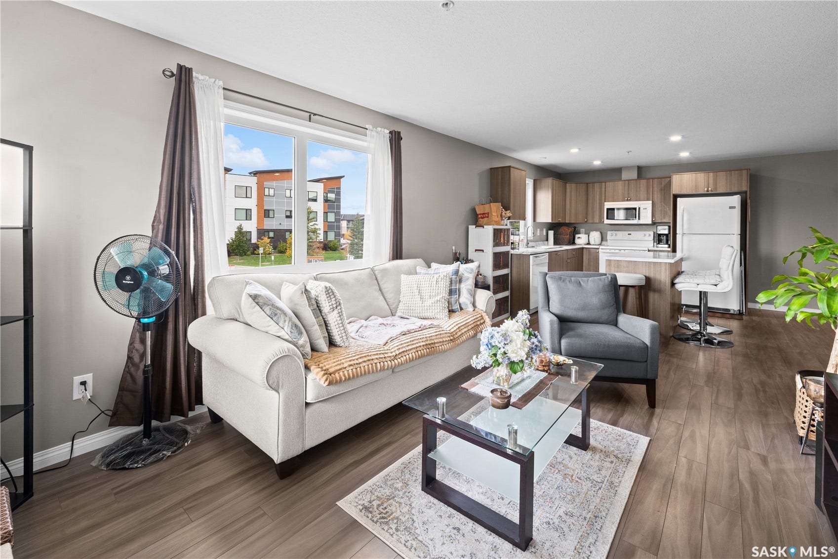 Open-concept living area featuring wood-finish flooring, a large window, recessed lighting, and a kitchen with wood-finish cabinetry and white appliances