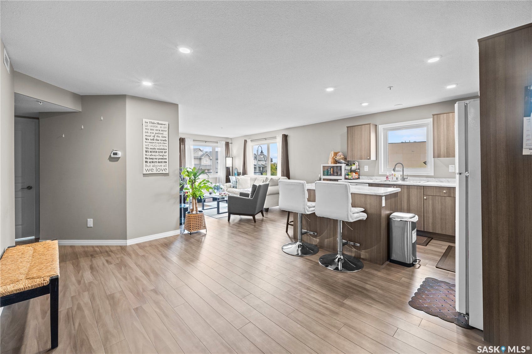 Open-concept layout featuring wood-finish flooring, recessed lighting, a kitchen island with seating, and a stainless steel sink
