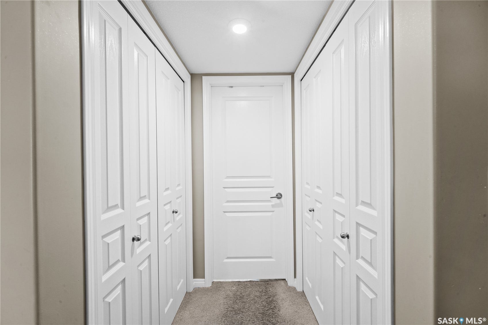 Recessed lighting illuminates the hallway featuring a paneled door and bi-fold closet doors with chrome hardware