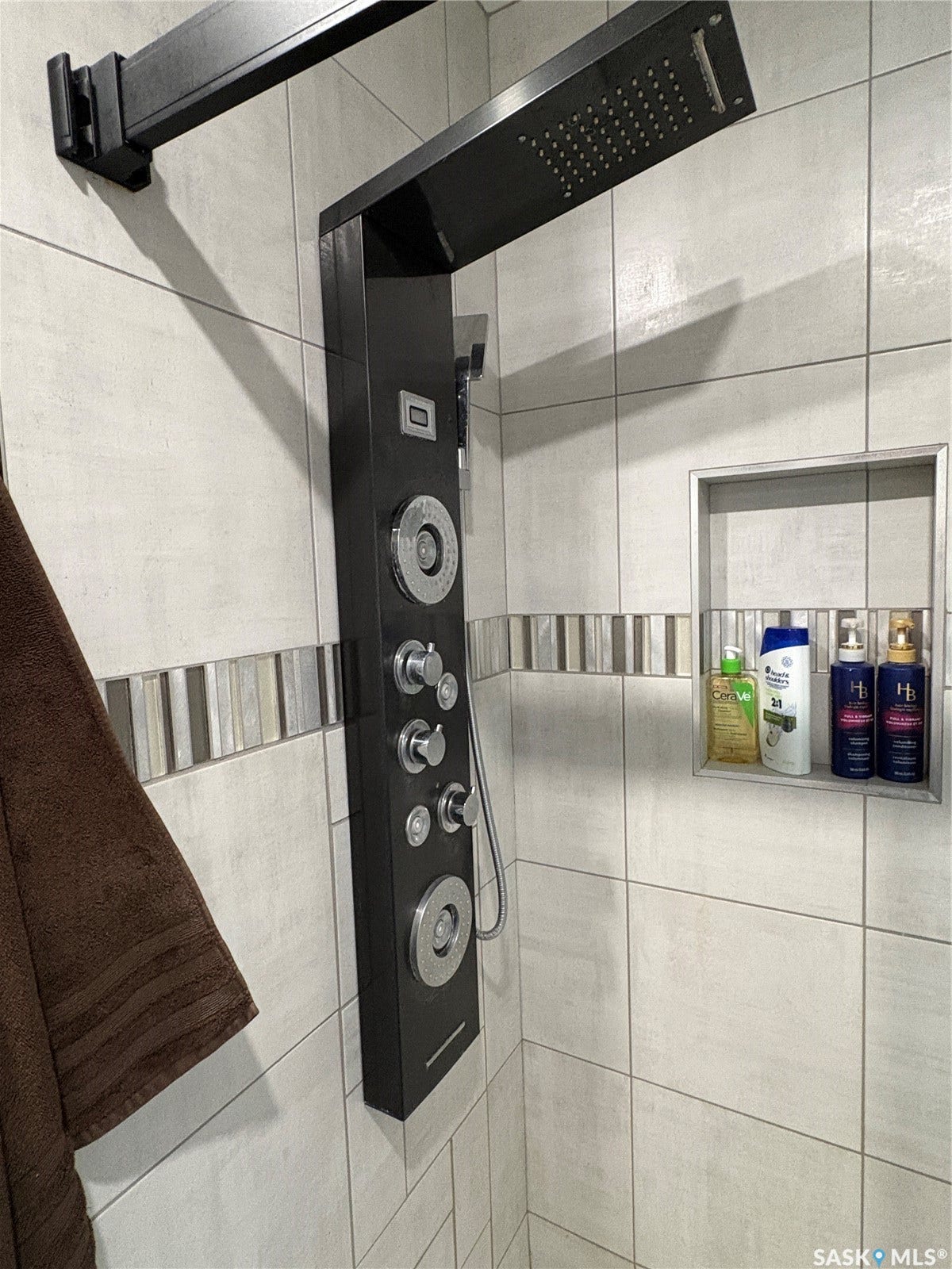 Modern shower panel with multiple spray settings and a handheld shower, light-toned rectangular wall tiles, horizontal mosaic accent tiles, and a recessed shower niche