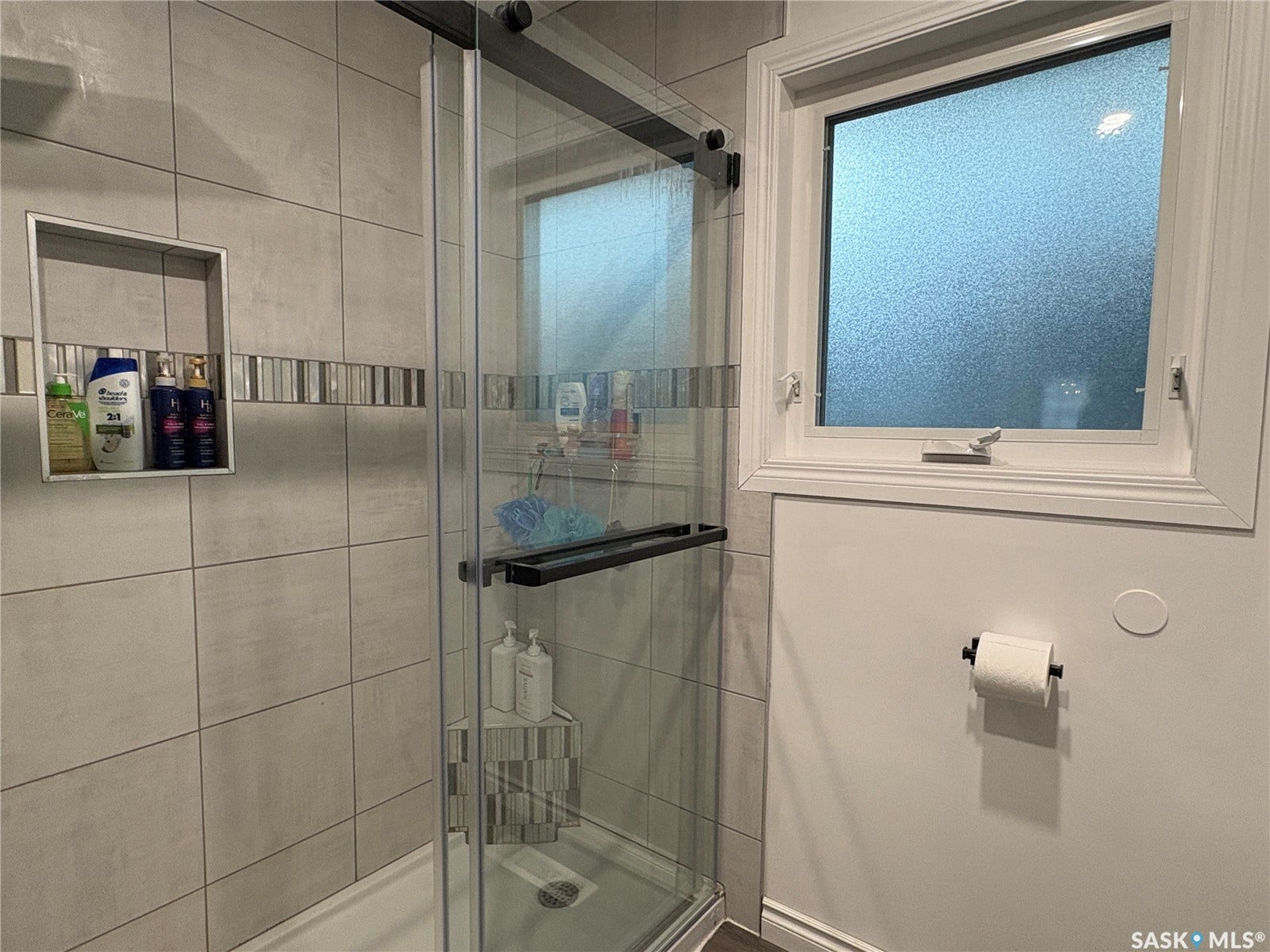 Glass-enclosed shower with a sliding door, tiled walls featuring a decorative accent band, and an integrated shower niche