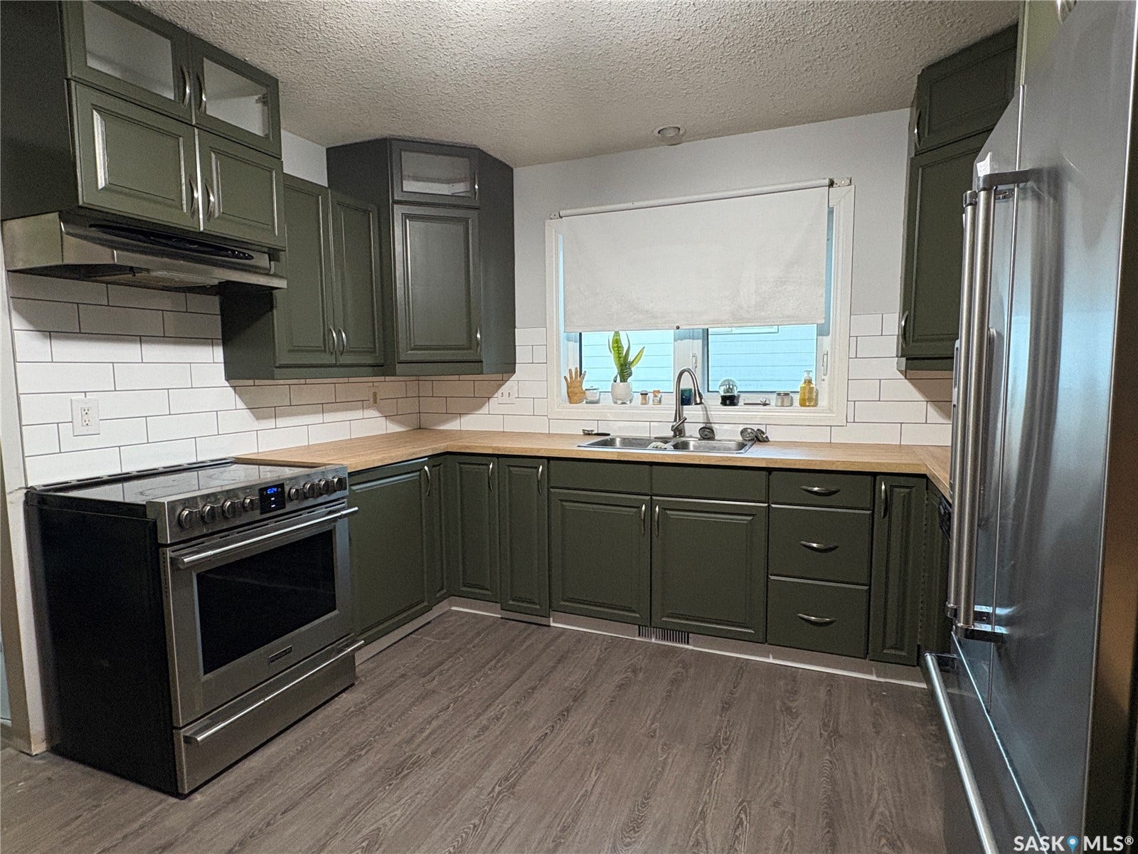 Kitchen featuring dark green cabinetry, a stainless steel electric range, wood-finish countertops, subway tile backsplash, and a large window