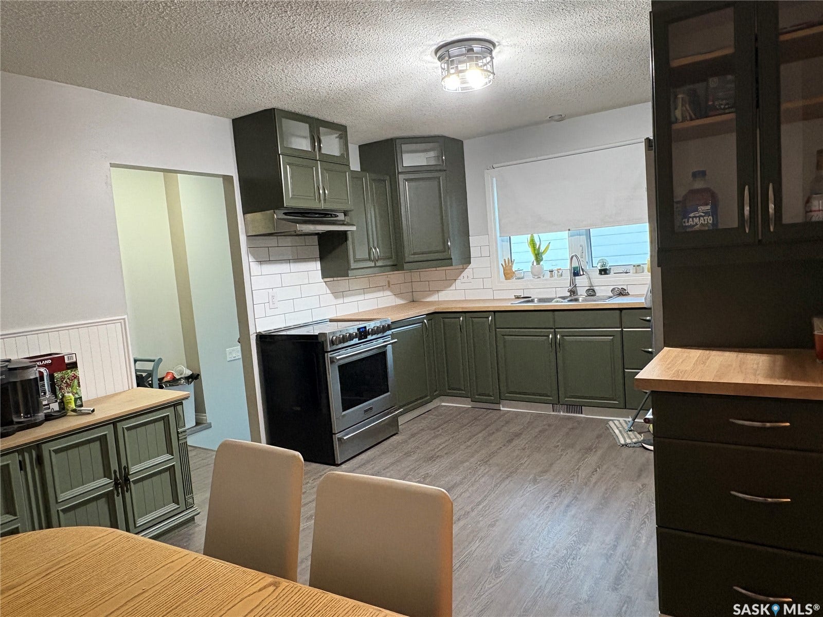 Kitchen featuring dark green cabinetry, wood-finish countertops, stainless steel range, white subway tile backsplash, and wood-finish flooring