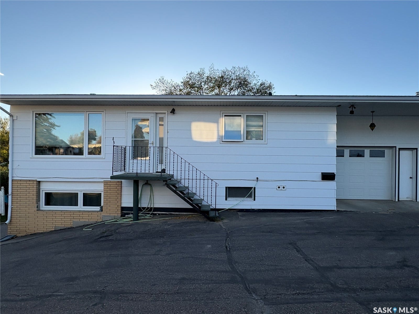 White siding exterior with a single garage door, a side entrance, and a front entry staircase with metal railing
