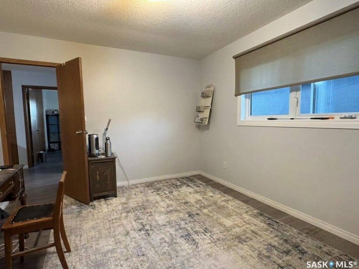 Wood-finish flooring with white trim, a window with a roller shade, and a wood-paneled door frame