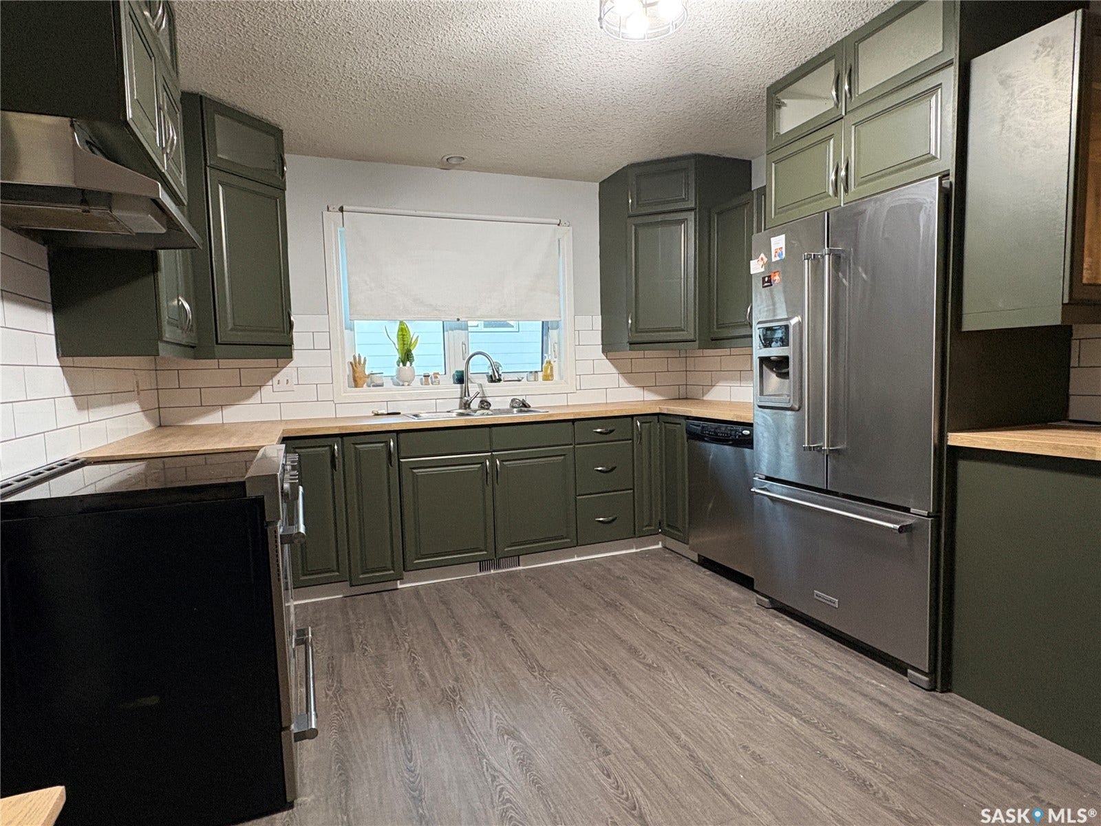Kitchen featuring wood-finish flooring, dark green cabinetry, light wood-finish countertops, and white subway tile backsplash