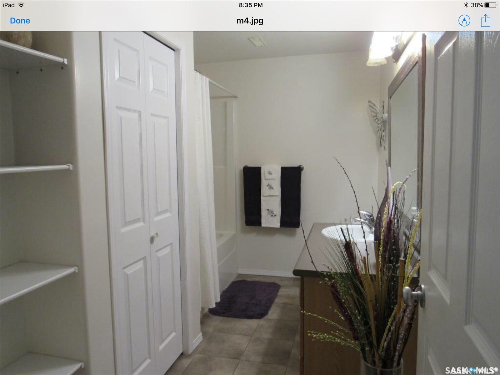 White paneled bi-fold door, built-in shelving, tiled flooring, vanity with dark countertop, and integrated bathtub with shower