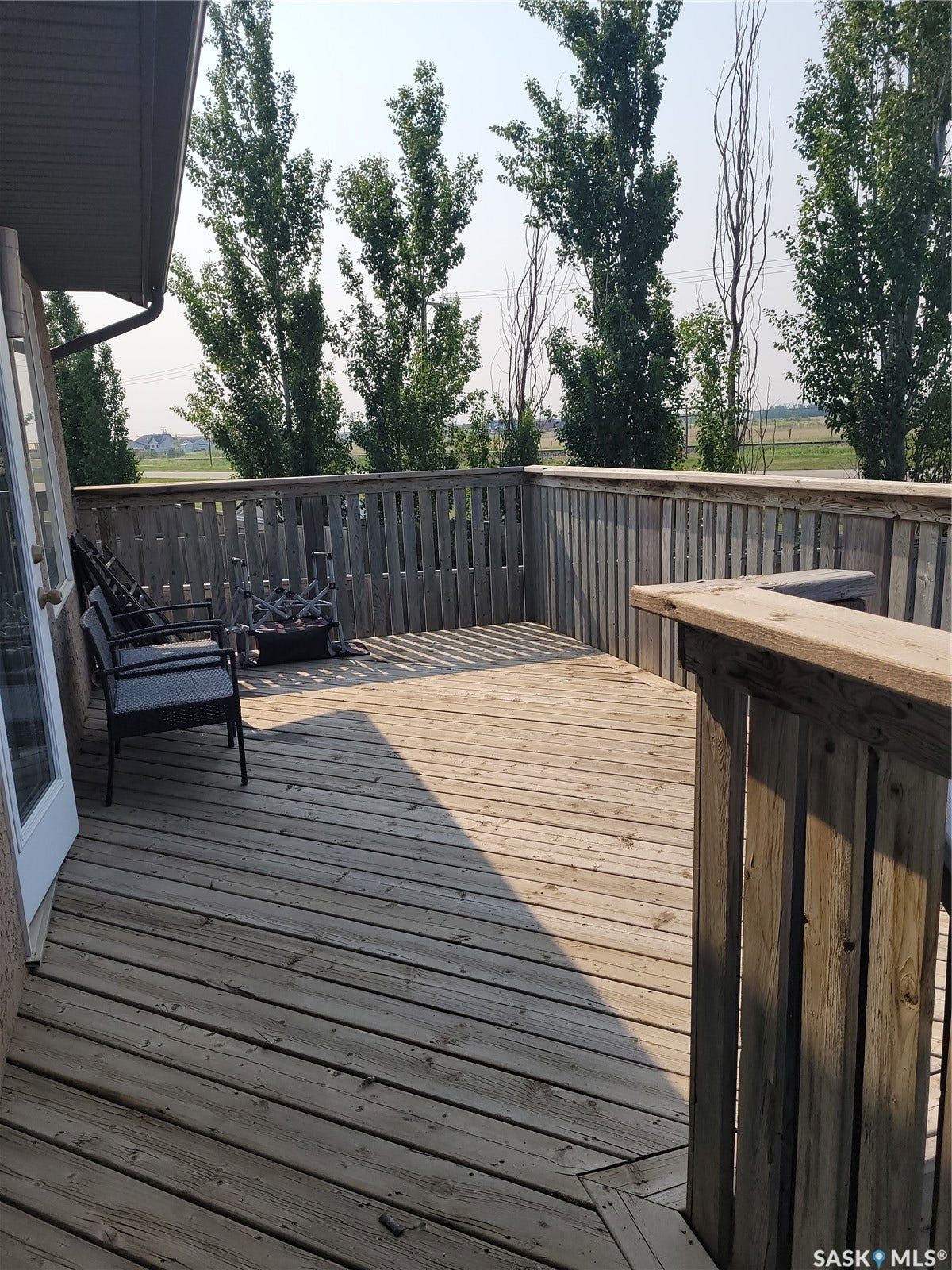 Expansive wood deck with a full wood railing, double patio doors, and mature trees beyond