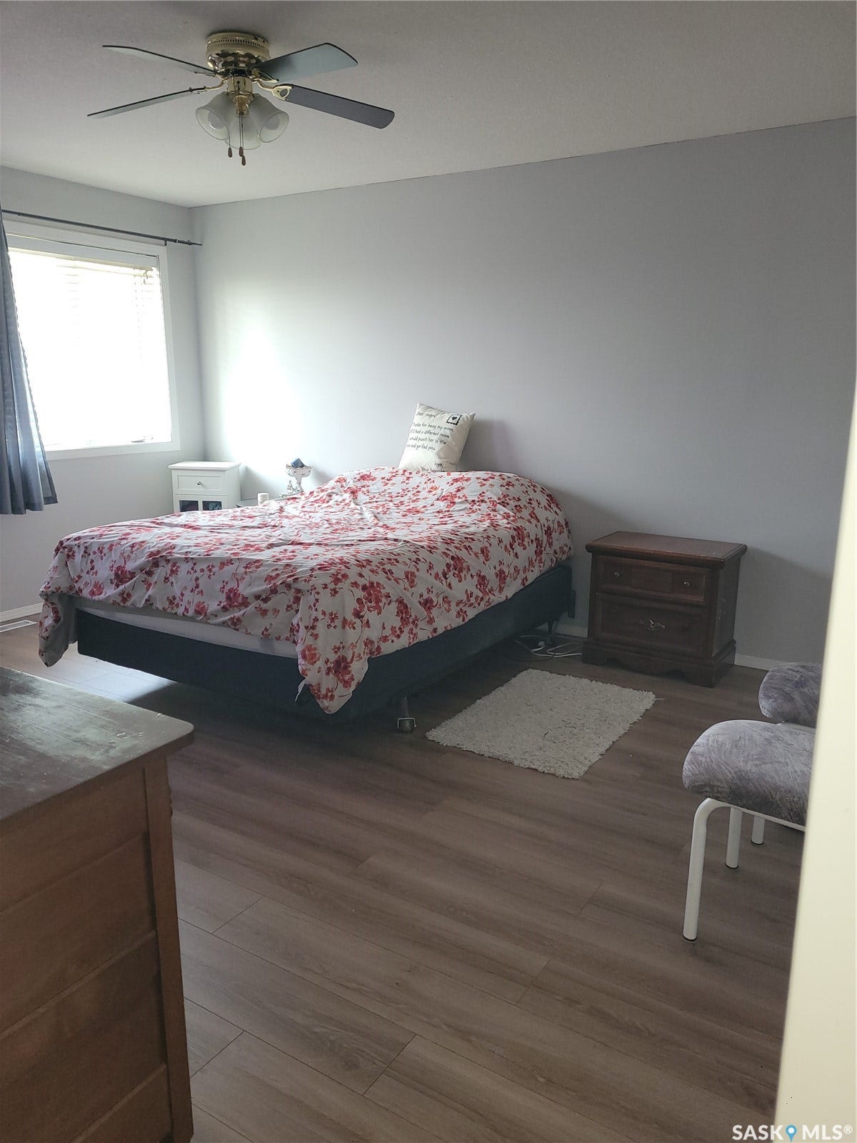 Wood-finish flooring throughout, ceiling fan with integrated lighting, window with horizontal blinds, and neutral wall paint