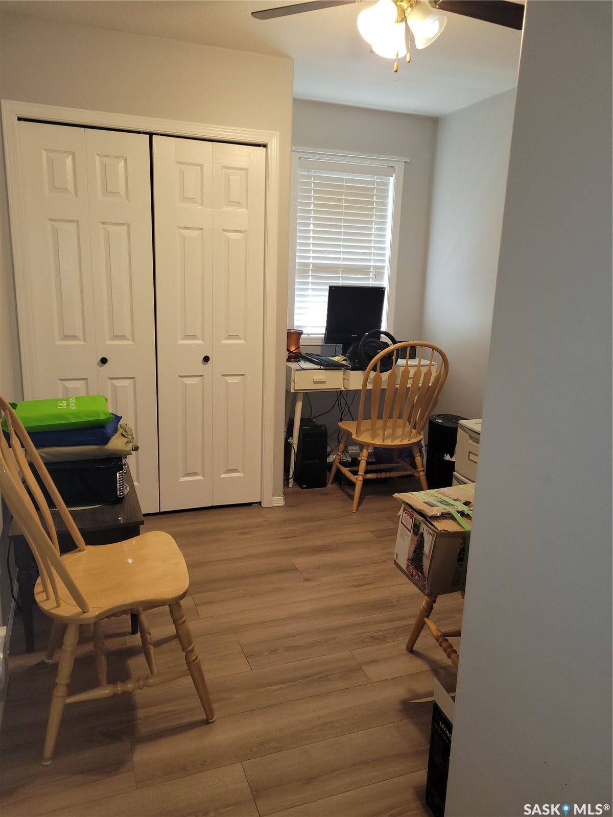 Wood-finish flooring, white bi-fold closet doors, ceiling fan with light fixture, and window with blinds