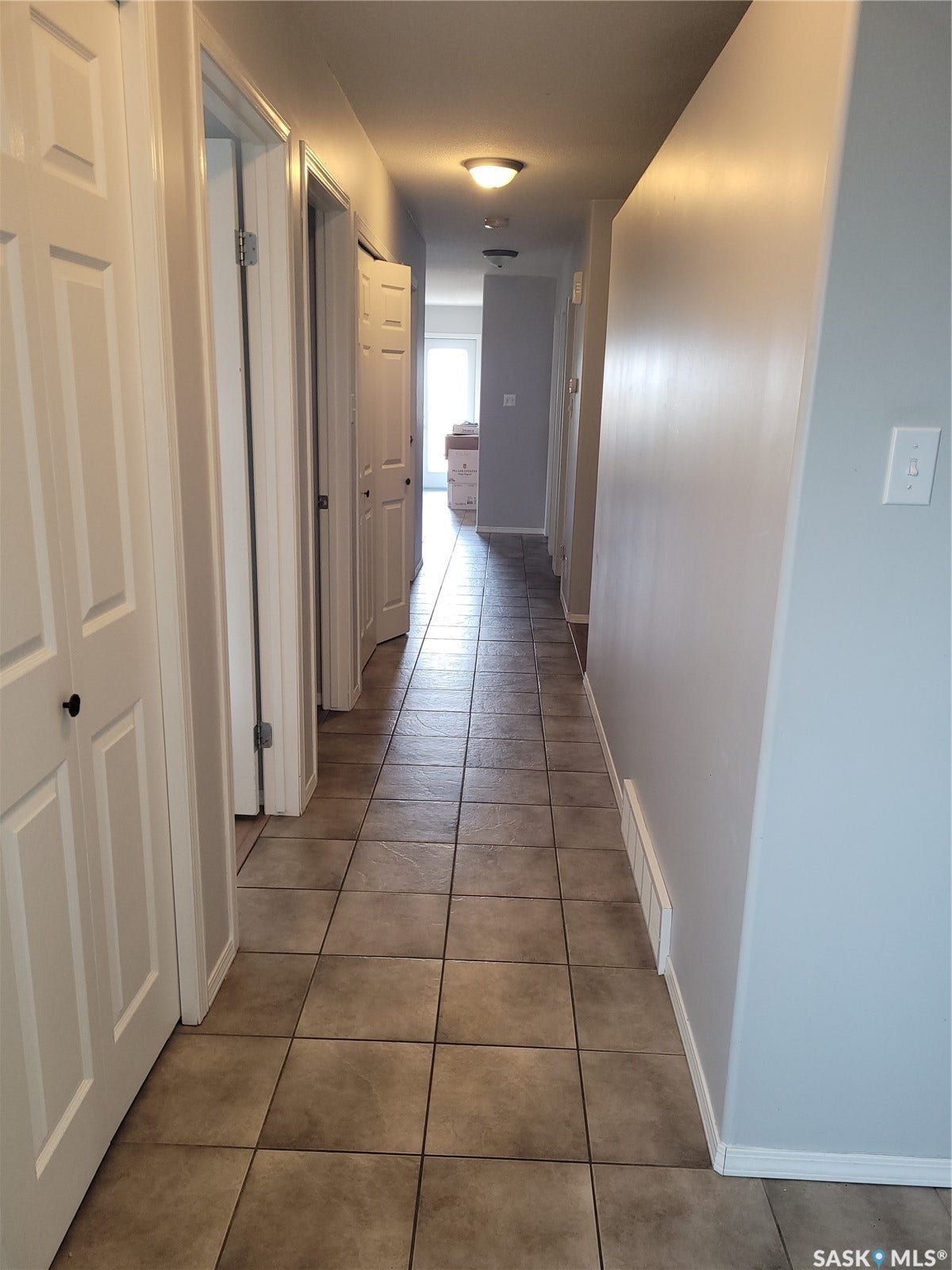 Hallway featuring tile flooring, neutral wall tones, white panel doors, and flush-mount lighting
