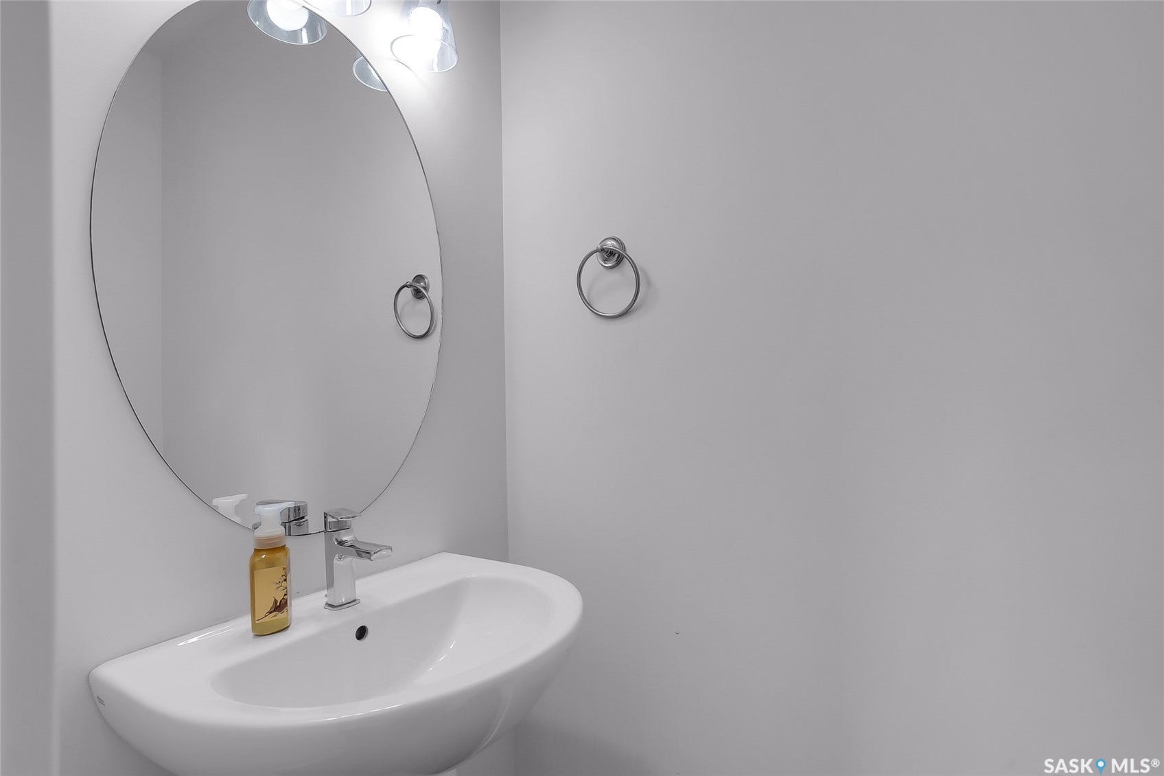 Pedestal sink with a polished chrome faucet, oval mirror, and wall-mounted light fixture