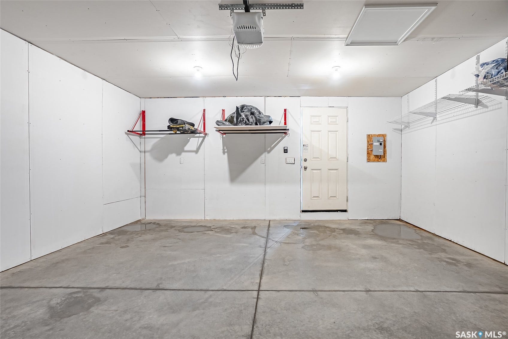 Concrete flooring, white paneled walls, overhead lighting, door access, and built-in shelving
