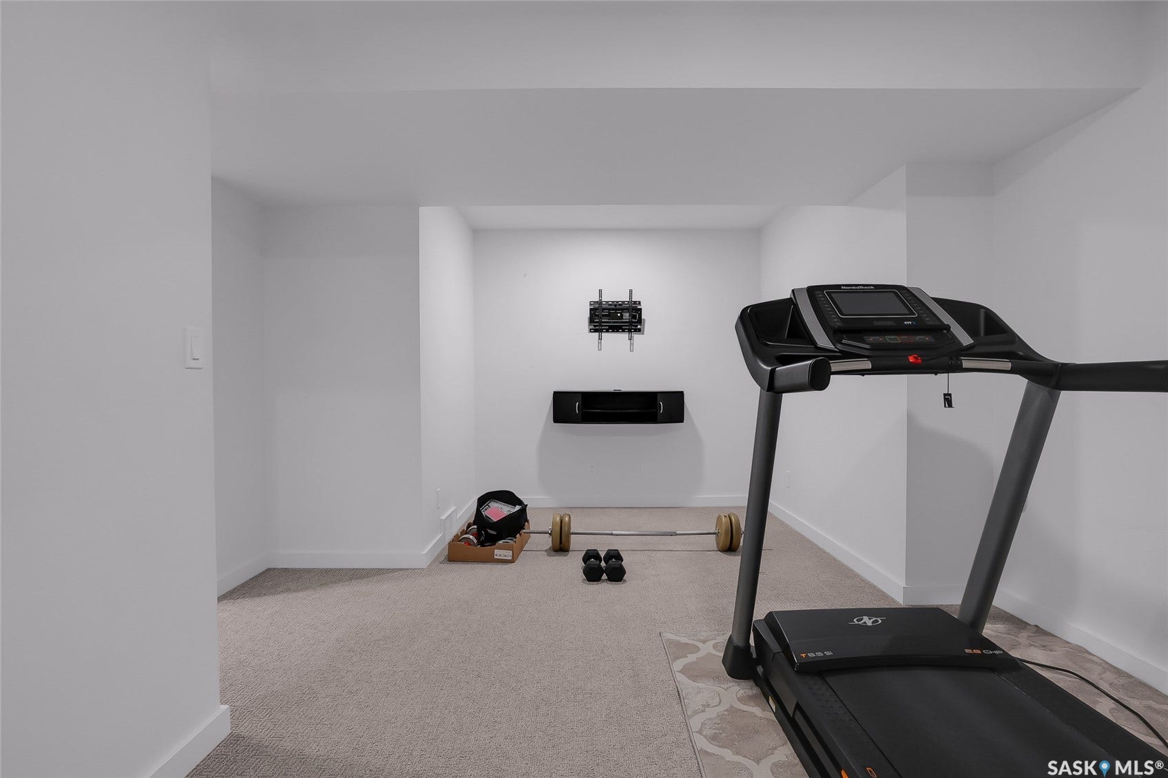 Carpeted flooring with white baseboards and walls, featuring a wall-mounted media bracket and floating shelf