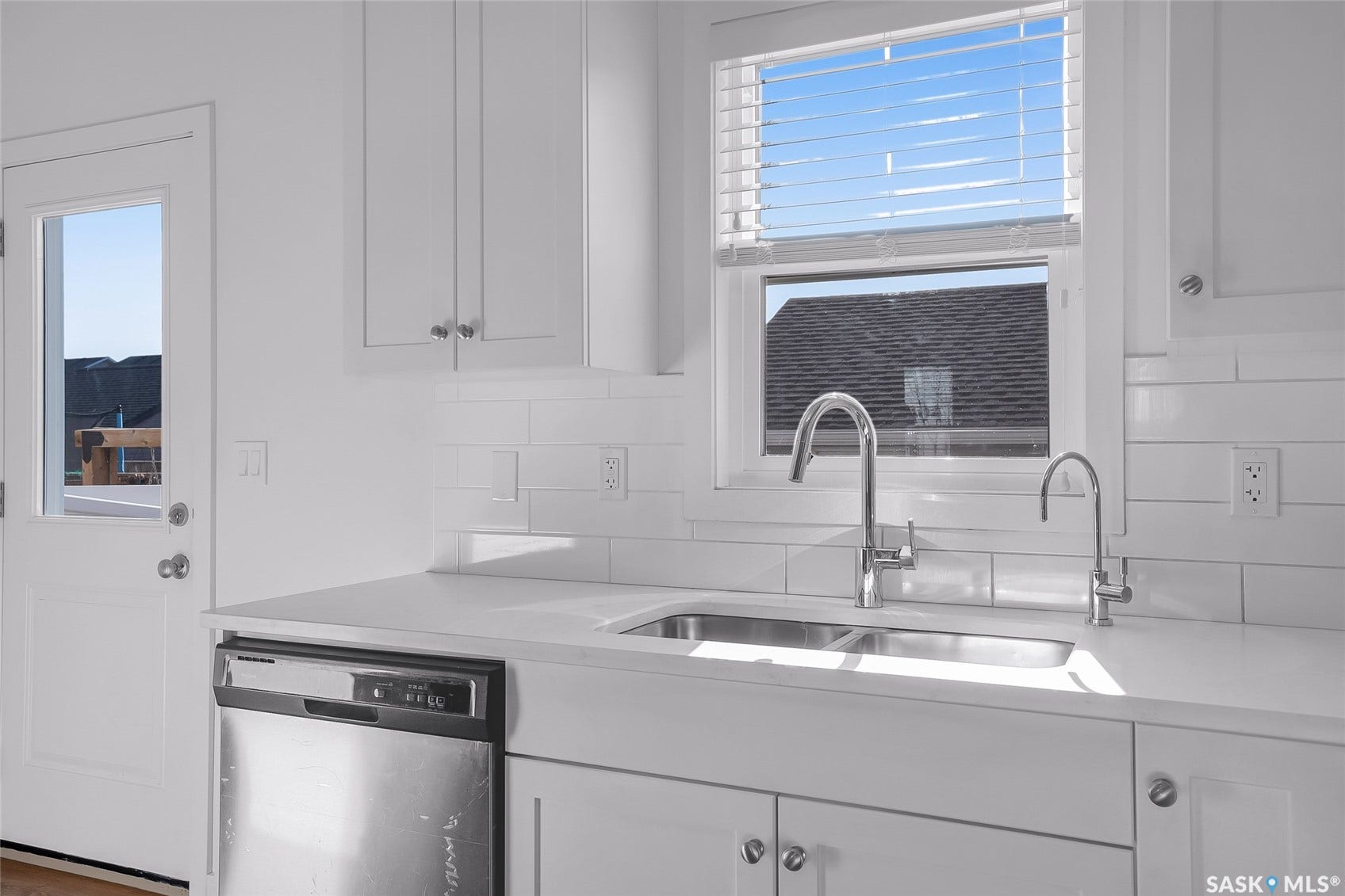 White shaker cabinetry, stainless steel dishwasher, dual basin sink, chrome fixtures, and a subway tile backsplash