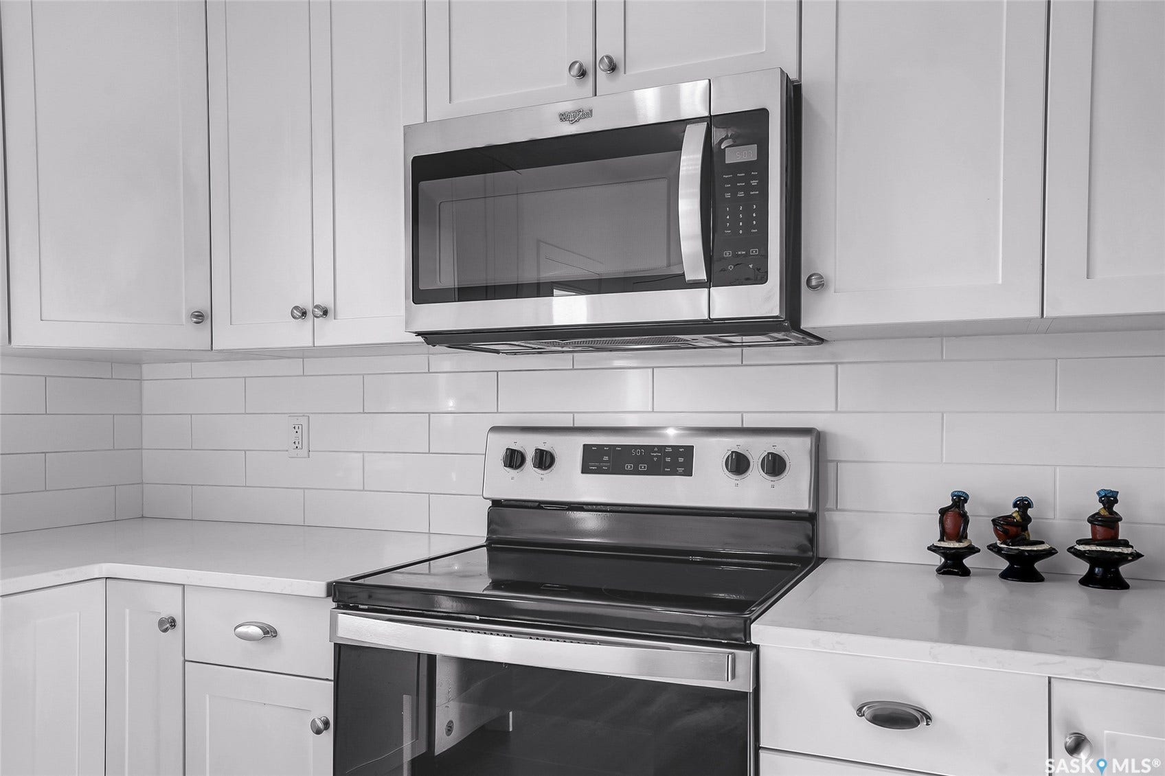 White shaker cabinetry with chrome hardware, subway tile backsplash, stainless steel microwave, and built-in electric range