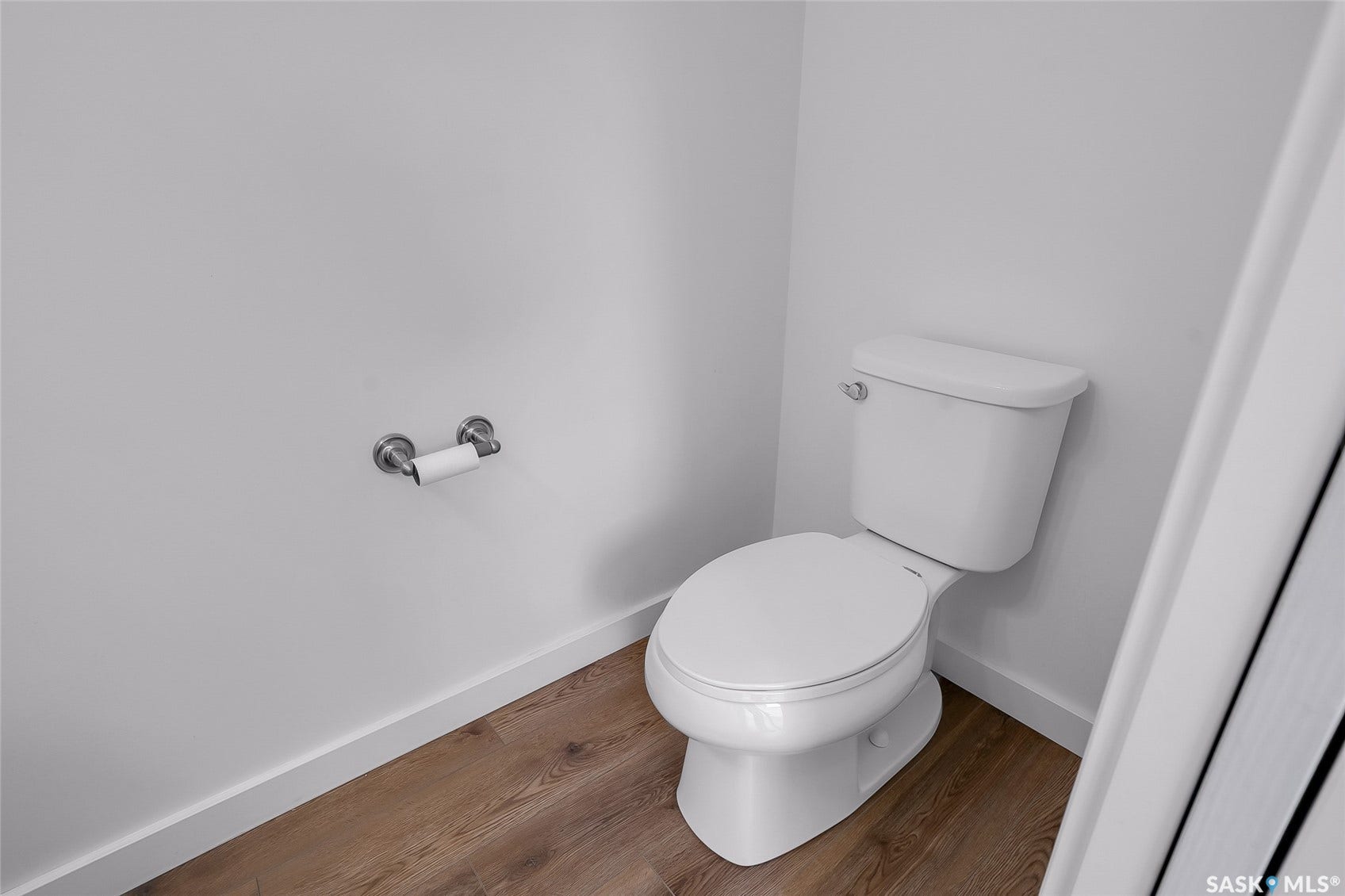 White two-piece toilet, wood-finish flooring, and a chrome toilet paper holder