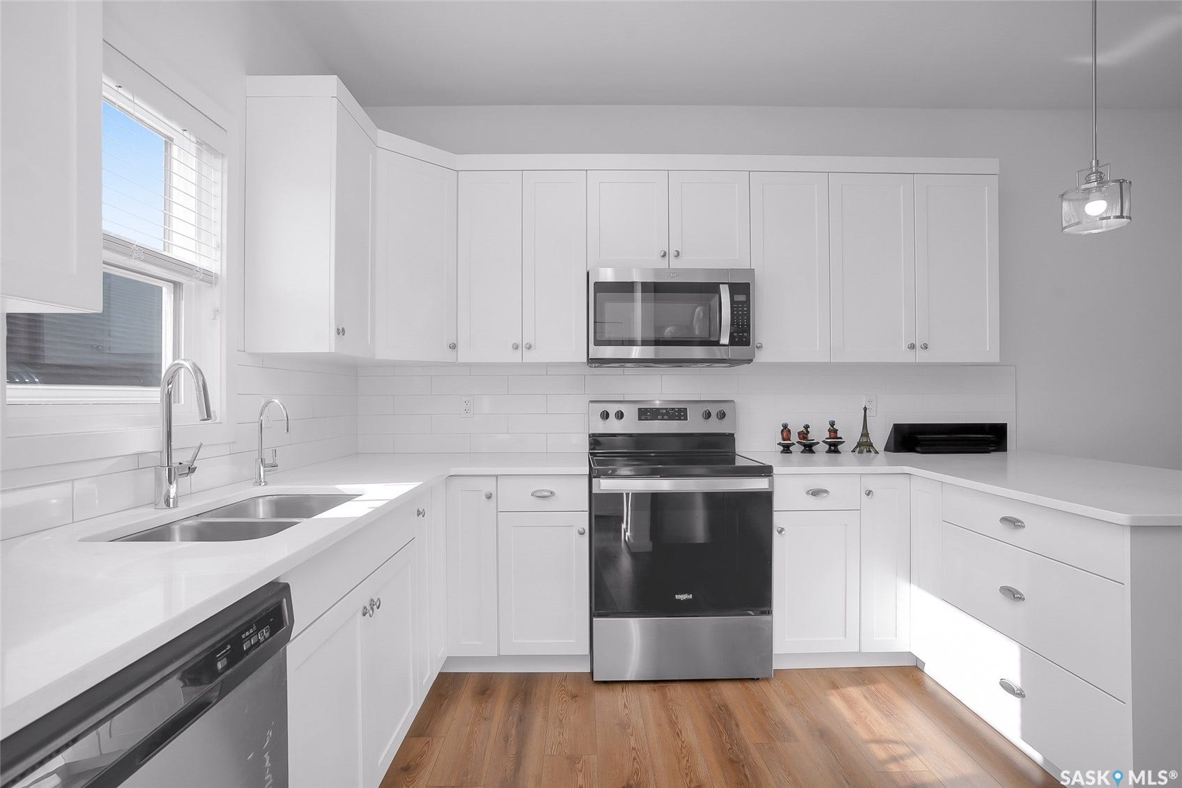 White cabinetry with brushed nickel hardware, stainless steel appliances, dual basin sink, white subway tile backsplash, and wood-finish flooring