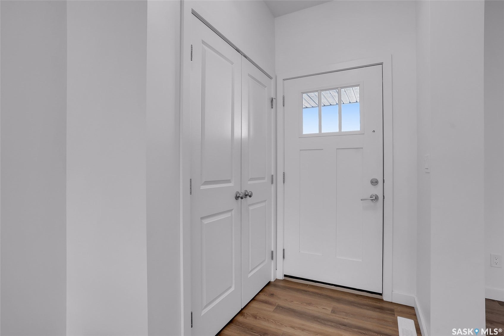 Entryway featuring wood-finish flooring, a white paneled entry door with decorative glass, and white bi-fold closet doors