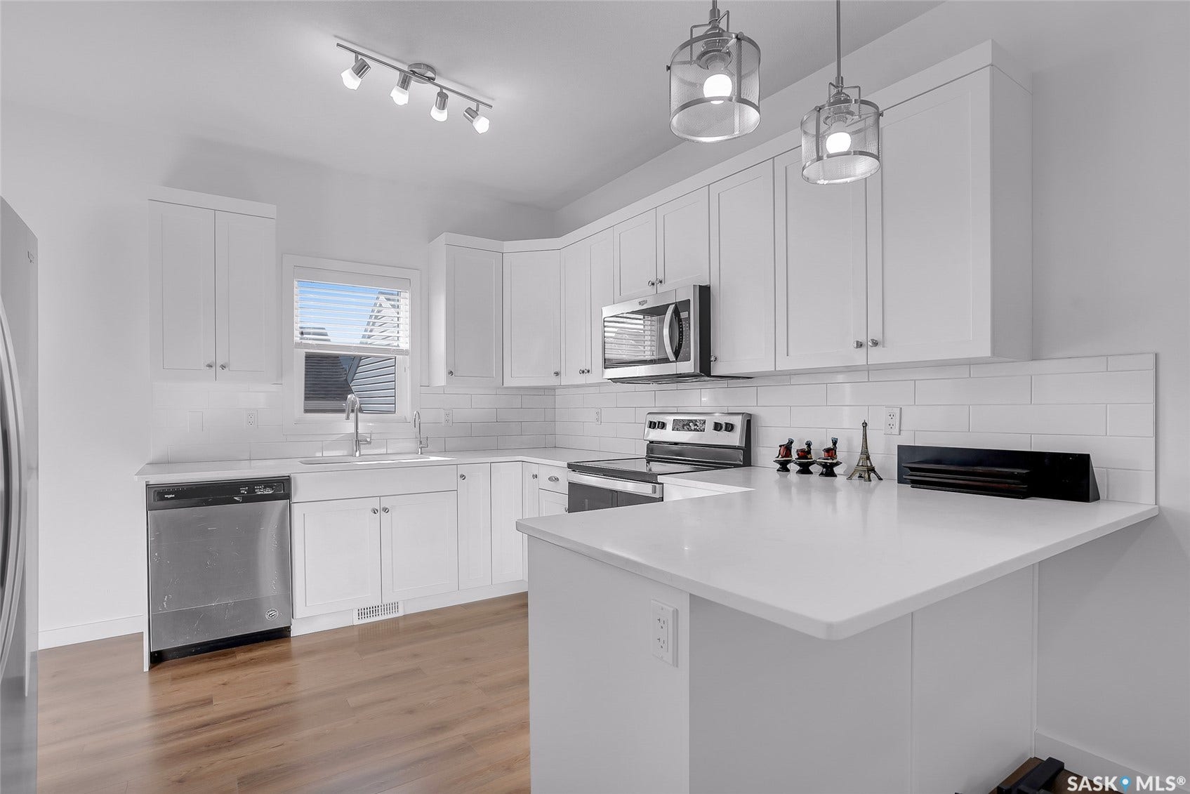 Modern kitchen with wood-finish flooring, white cabinetry, stainless steel appliances, white subway tile backsplash, and white countertops