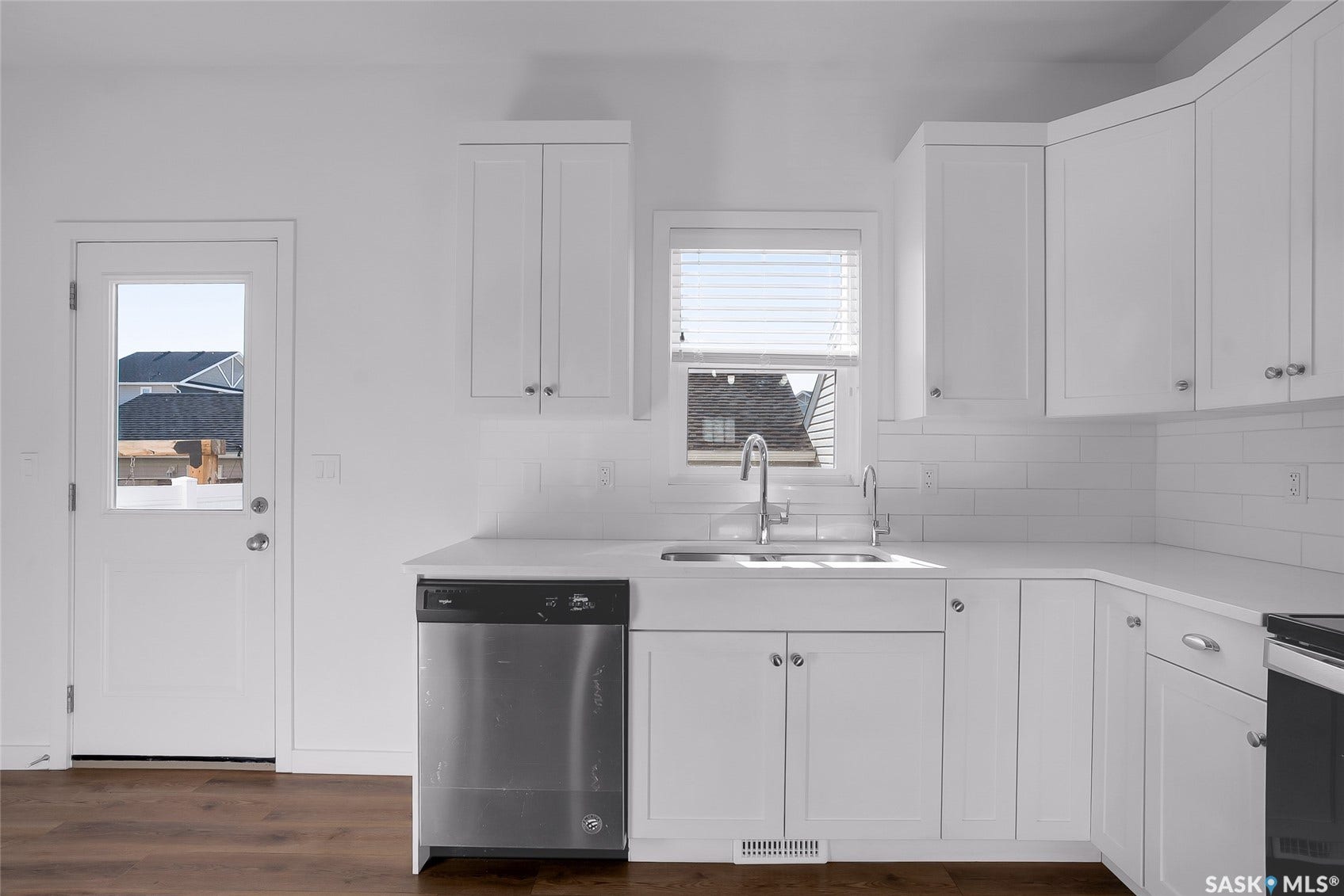 White shaker-style cabinetry with chrome hardware, subway tile backsplash, stainless steel dishwasher, and wood-finish flooring