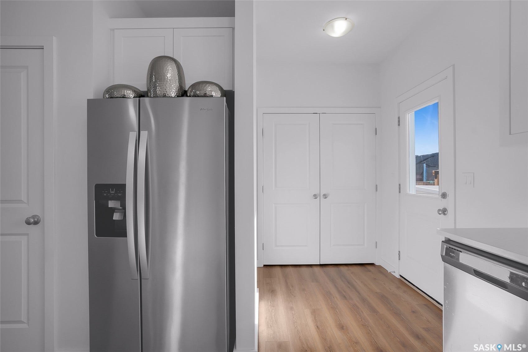 Stainless steel side-by-side refrigerator, white cabinetry, wood-finish flooring, white paneled doors, and a door with a window