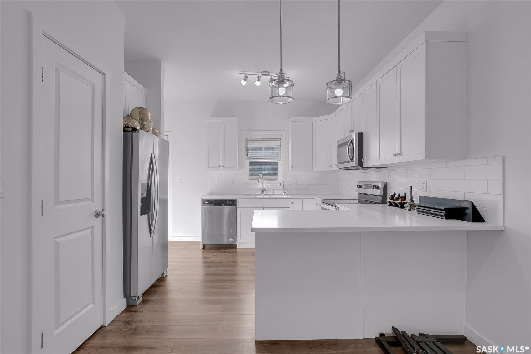 Kitchen featuring white shaker cabinetry, stainless steel appliances, wood-finish flooring, white subway tile backsplash, and pendant lighting
