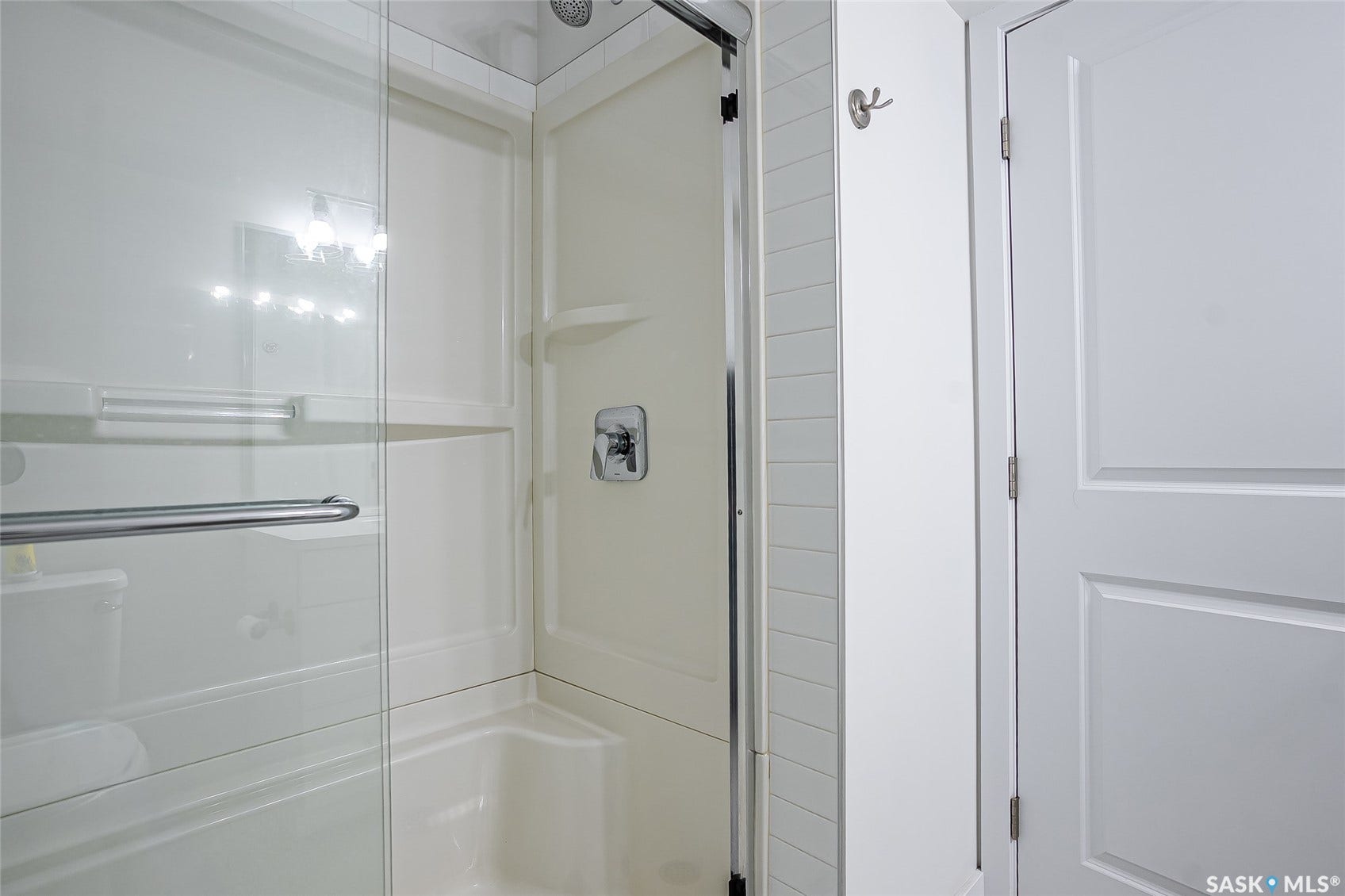 Shower/tub combination with glass enclosure, chrome fixtures, and built-in shelving