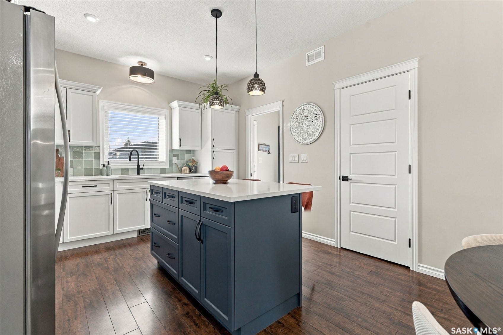 919 Kolynchuk Bend, Saskatoon SK S7T 0V9 Kitchen featuring a two-tone island with a light-colored countertop, dark wood-finish flooring, white cabinetry, and stainless steel appliances
