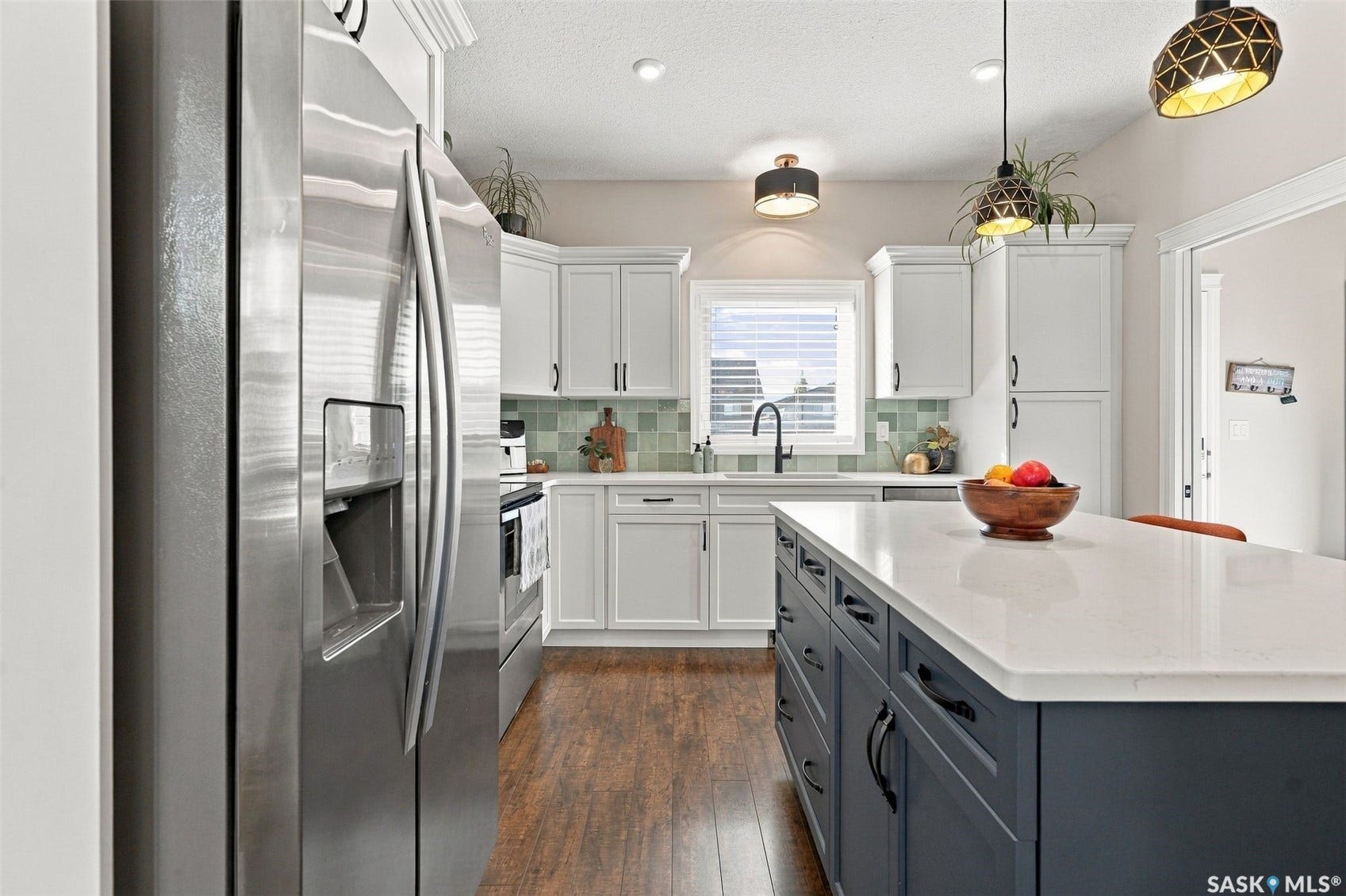 919 Kolynchuk Bend, Saskatoon SK S7T 0V9 Stainless steel refrigerator, wood-finish flooring, white cabinetry, dark blue kitchen island with a light-toned countertop, and pendant lighting fixtures