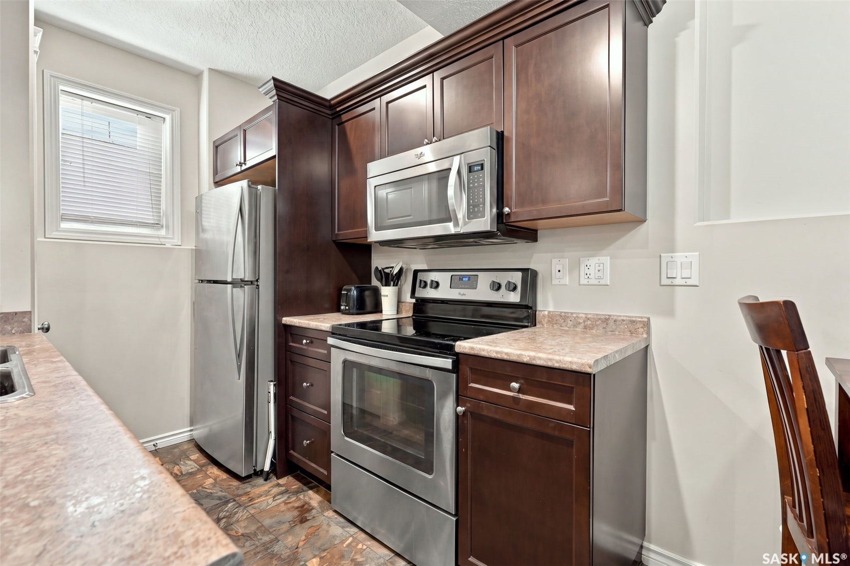 919 Kolynchuk Bend, Saskatoon SK S7T 0V9 Kitchen featuring dark wood-finish cabinetry, stainless steel appliances, and durable laminate countertops
