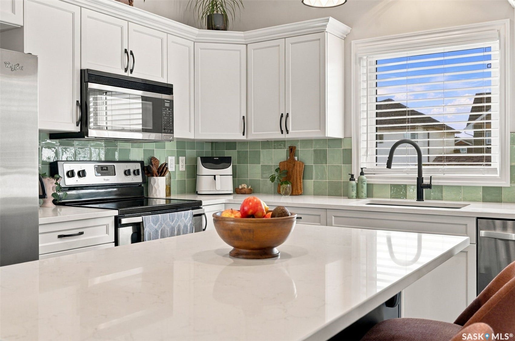 919 Kolynchuk Bend, Saskatoon SK S7T 0V9 White cabinetry, integrated stainless steel appliances, patterned green tile backsplash, white countertops, and a black gooseneck faucet