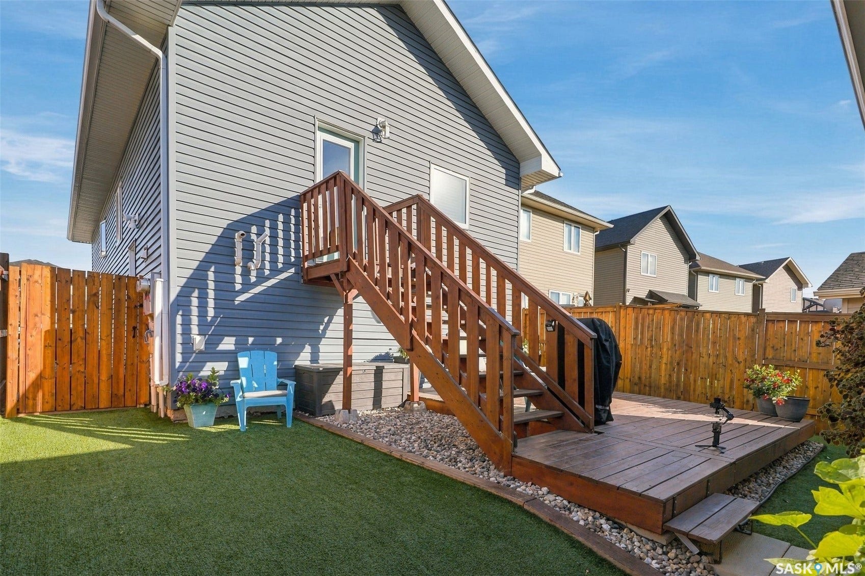 919 Kolynchuk Bend, Saskatoon SK S7T 0V9 Exterior featuring gray siding, a wood deck with stairs, artificial turf landscaping, and wood privacy fencing